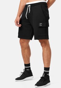 Shorts en coton noirs avec taille élastique à cordon, poches latérales et une poche cargo sur la jambe droite avec un écusson logo circulaire.