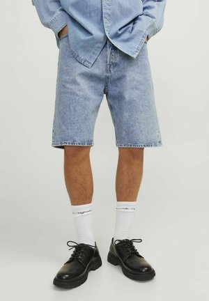 Pantalones cortos de mezclilla azul claro con un corte relajado. Combinados con calcetines blancos y zapatos negros con cordones. Los materiales parecen ser a base de algodón con costuras estándar.