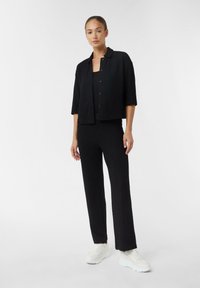 Czarna, wyszywana w jodełkę krótka kurtka z krótkimi rękawami, zestawiona z pasującymi spodniami i białymi trampkami. Prosty zamek na guziki.