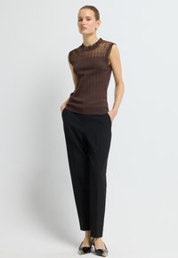Brązowy prążkowany top bez rękawów z przezroczystym detalem przy dekolcie, połączony z czarnymi eleganckimi spodniami i czarnymi szpilkami z złotymi akcentami.