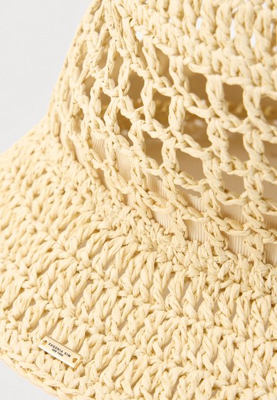 Πλεχτό καπέλο από άχυρο σε ανοιχτό κίτρινο χρώμα, με ανοιχτό σχέδιο υφής, φαρδύ γείσο και υφή με ανάγλυφο φινίρισμα. Διακοσμημένο με μια μικρή ετικέτα με το λογότυπο της μάρκας.