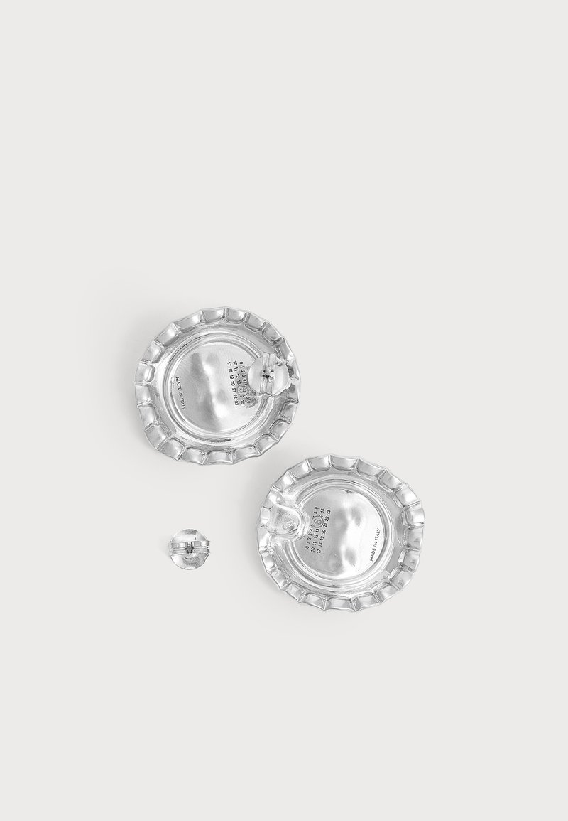 Deux broches rondes en argent avec des bords festonnés et une petite broche ronde sur fond blanc, avec des attaches visibles.