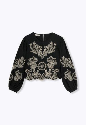 Blouse noire avec de longues manches bouffantes, ornée d'une broderie beige complexe en motifs floraux et circulaires, et d'une fermeture par clé à l'arrière.