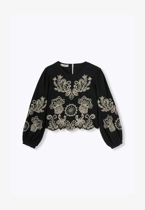 Blouse noire avec de longues manches bouffantes, ornée d'une broderie beige complexe en motifs floraux et circulaires, et d'une fermeture par clé à l'arrière.