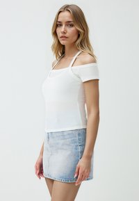 Biała, prążkowana bluzka z krótkim rękawem w stylu off-the-shoulder, w połączeniu z jasnoniebieską mini spódnicą dżinsową. Gładka tekstura i dopasowany fason.