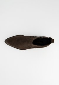 Botín de ante marrón con punta puntiaguda, detalles en relieve, cremallera lateral y superficie texturizada.