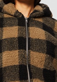 Brun- og sortternet fleece-hoodie med lynlås og tekstureret stof. Har en hætte og en blød, fuzzy overflade.