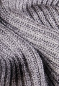 Nahaufnahme eines weichen, grauen Strickstoffs mit Rippen- und Zopfmuster, die strukturierte Falten erzeugen.