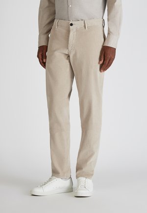 Beige Corduroyhosen mit vertikalen Streifen, frontalen Taschen, einem Knopfverschluss und geradem Bein, kombiniert mit weißen Sneakern.