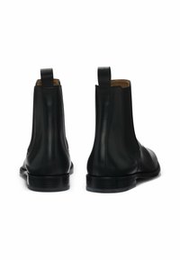 Czarne skórzane botki Chelsea z elastycznymi bokami, pętlami do zakładania i płaskimi obcasami. Gładka faktura i elegancki, minimalistyczny design.