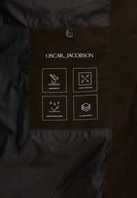 L'etichetta della giacca impermeabile marrone presenta icone che mostrano le proprietà antivento, elasticità a quattro vie, idrorepellenza e tessuto a tre strati.