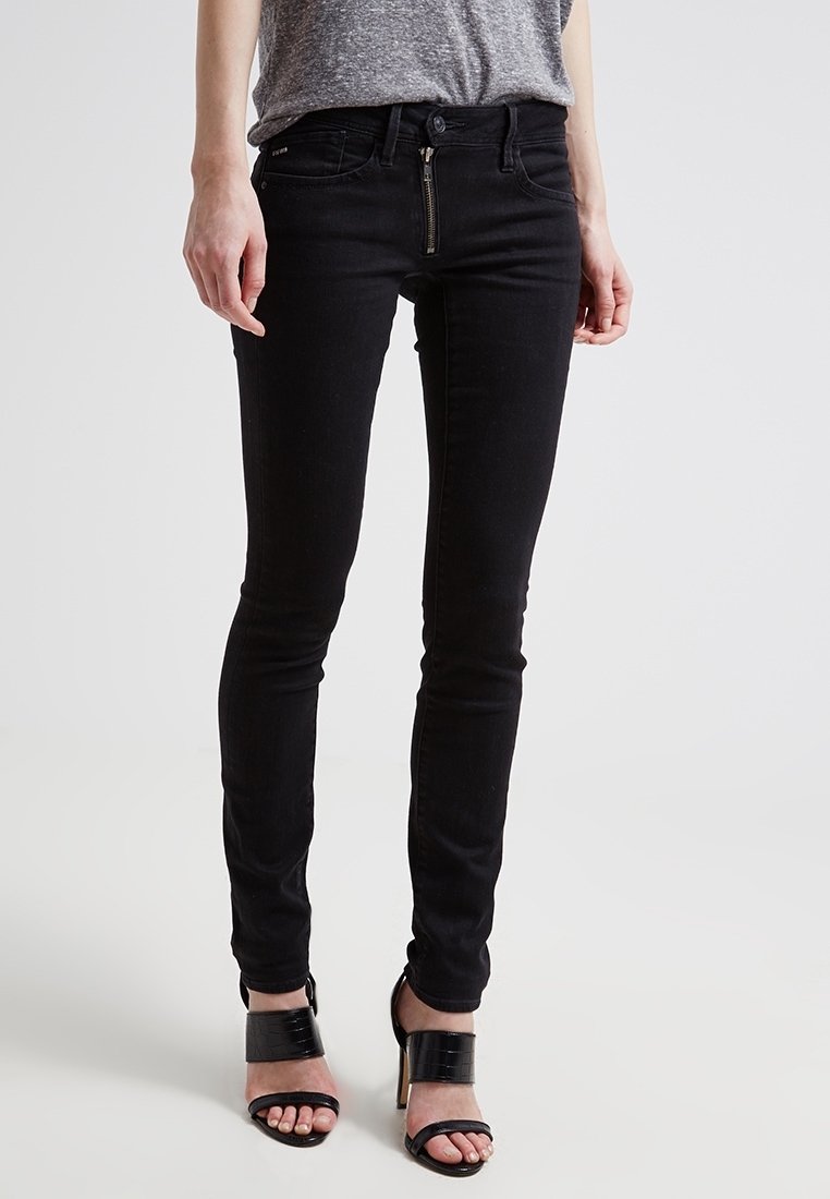Black skinny jeans made of denim, featuring a zip fly, front pockets, and a smooth texture. Paired with strappy black heels.