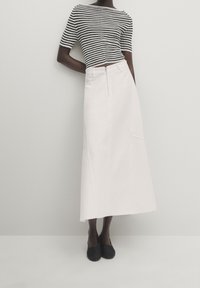 Mörkhyad person som bär en svart och vit horisontellt randig kortärmad topp, högmidjad vit midikjol och svarta slip-on skor.