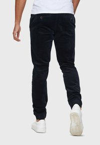 Pantalons en velours côtelé bleu marine avec une texture en relief, dotés de poches arrière avec boutons, de chevilles fuselées et de baskets blanches.