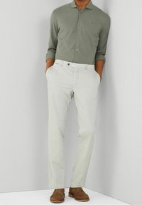 Chandail long à manches vert clair, pantalon couleur crème et chaussures en daim marron. Le chandail a un col et des boutons ; le pantalon est de coupe ajustée.