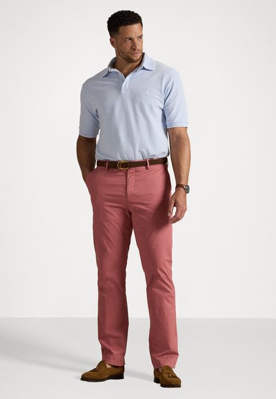 Polo shirt de culoare albastru deschis cu mâneci scurte, pantaloni roz, curea maro și încălțări mocasini maro. Branding minim pe cămașă.