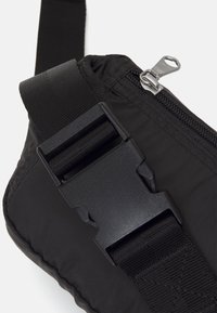 Schwarze Nylon-Schultertasche mit einem glänzenden Reißverschluss, einem Kunststoffschnallenverschluss und einem verstellbaren Tragegurt; verfügt über eine strukturierte Oberfläche und ein schlankes Design.