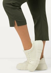 Baskets montantes blanches avec une semelle épaisse, des lacets et des accents texturés. Pantalons cropped vert olive avec des fentes latérales.