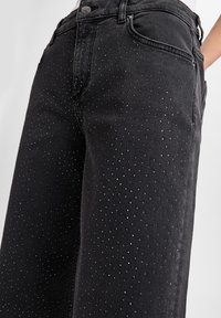 Czarne dżinsy z denimu z małymi metalowymi ćwiekami ułożonymi w wzór kropek, z klasycznym pięciokomorowym krojem i standardowym paskiem.