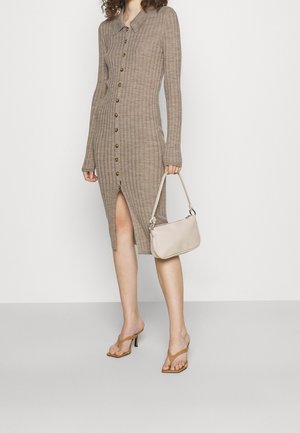 Langes, geripptes Strickkleid in Hellbraun mit Kragen, Knöpfen vorn und einem seitlichen Schlitz. Kombiniert mit einer hellbeigen Handtasche und braunen, hochhackigen Sandalen.