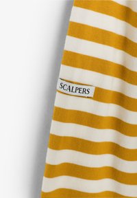 Camisa de algodón a rayas con rayas alternas amarillas y blancas, que cuenta con una pequeña etiqueta rectangular con "SCALPERS" bordada en negro.