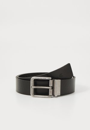 Cintura in pelle nera con fibbia rettangolare in argento, caratterizzata da una superficie liscia e logo "CK" in rilievo sulla striscia.