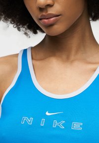 Gros plan sur une femme portant un débardeur Nike bleu avec des bordures blanches et un petit logo Nike au-dessus du nom de la marque.