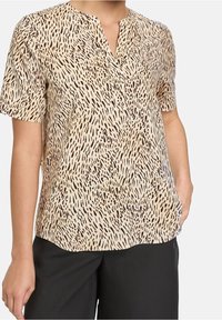 Blouse à manches courtes en tissu beige clair avec un motif à points noirs. Caractérisée par un décolleté en V et une coupe décontractée.