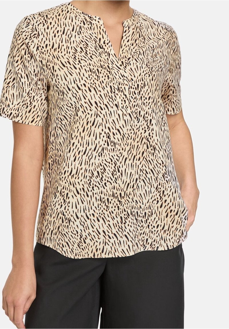Blouse à manches courtes en tissu beige clair avec un motif à points noirs. Caractérisée par un décolleté en V et une coupe décontractée.