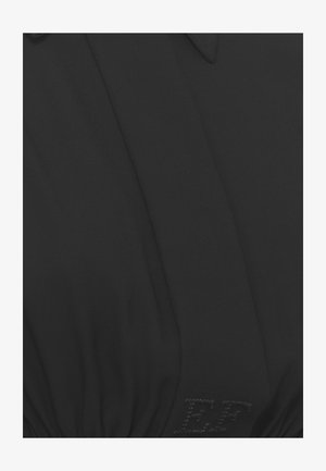 Primo piano di tessuto nero con lettere "EF" cucite e cucitura visibile con arricciature vicino al fondo, suggerendo un dettaglio del capo.