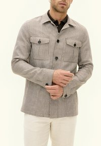 Brown and beige plaid patterned jacket with four front pockets, button closures, and a smooth fabric texture. Long sleeves with button cuffs.