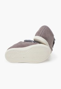 Scarpe in suede grigio con una texture morbida, caratterizzate da una forma curvata, una suola in gomma bianca e una fascia in velcro sul lato per una facile chiusura.