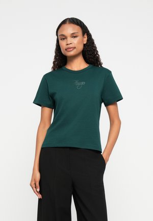 Tricou verde cu mânecă scurtă, din bumbac, cu guler rotund și un logo subtil pe piept. Asortat cu pantaloni negri.