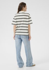 Polo rayé en crème avec des rayures noires, associé à un jean large bleu clair. Présente un col et des manches courtes.