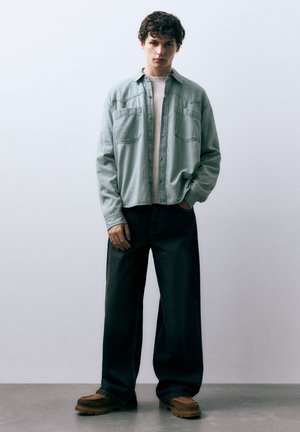 Világoskék kord ing fehér póló fölött, sötét bősz szabású farmerrel és barna lábbelivel párosítva. Az ing két mellzsebbel rendelkezik.