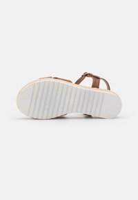 Brown sandal with a textured tan upper, adjustable strap, and a white rubber outsole featuring horizontal grooves for traction.