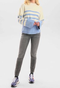 Pull rayé bleu clair et crème avec des manches larges, associé à un jeans gris et des baskets violettes. La texture semble douce et confortable.