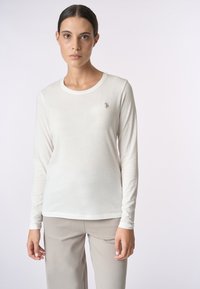 Maglia a maniche lunghe di un color crema chiaro, realizzata in materiale morbido. Presenta un collo rotondo e un logo ricamato sul petto sinistro. Tessuto liscio.