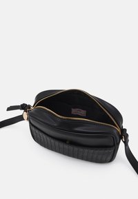 Zwarte crossbodytas met een glad leren bovenkant, een getextureerde geweven basis, een gouden rits en een leren band. Het interieur heeft een logolabel.