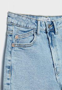 Jeans de mezclilla azul claro con bolsillos frontales, pasadores para cinturón, remaches de cobre, cierre de botón y una etiqueta visible "Mom Slim" en el interior de la cinturilla.