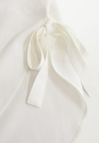 Weißer Stoff mit einer weichen Textur, versehen mit langen gebundenen Bändern. Einfaches Design mit klaren Linien und glatter Oberfläche.