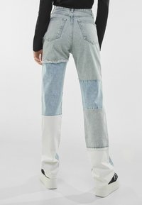 Jeans de mezclilla de lavado claro con un diseño de patchwork en paneles de azul claro, azul medio y blanco. Corte de pierna recta, dobladillos deshilachados y bolsillos traseros.