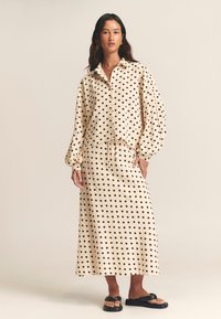 Polka dot outfit featuring a lightweight, beige fabric shirt with a collar and balloon sleeves, paired with a matching long skirt. Black polka dots.