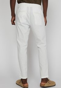 Pantalones de lino blancos con un corte relajado, cinturilla elástica y dos bolsillos traseros. Combinados con zapatos beiges sin cordones.