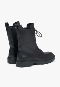 Czarne skórzane botki za kostkę mają sznurowane zapięcie, okrągły czubek i solidną podeszwę. Gładka faktura z przeszyciami po bokach.