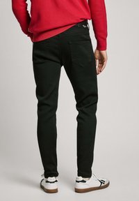 Black stretch jeans with a tapered fit, visible rear pockets, and minimal stitching, paired with white sneakers featuring brown soles.