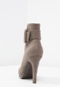 Stivale in camoscio color taupe con tacco a stiletto alto. Presenta una fibbia decorativa sul lato e una superficie liscia.