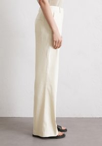 Hoge taille, wijde broek in lichtbeige linnen met zijzakken en een gladde textuur, gedragen met zwarte sandalen.