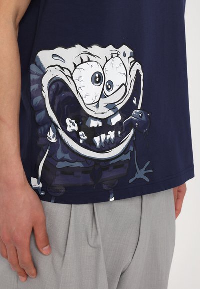 Mørkeblå t-shirt med et stort grafisk motiv af en tegneseriefigur med overdrevne ansigtstræk og en dryppende mund, korte ærmer.