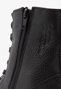 Zwarte leren enkellaars met een zijrits, een textuur op het oppervlak en decoratieve veters. Opvallend logo in het materiaal geperst.